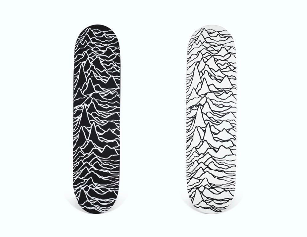A black and a white Supreme skateboard deck carrying the Unknown Pleasures pulse graphic